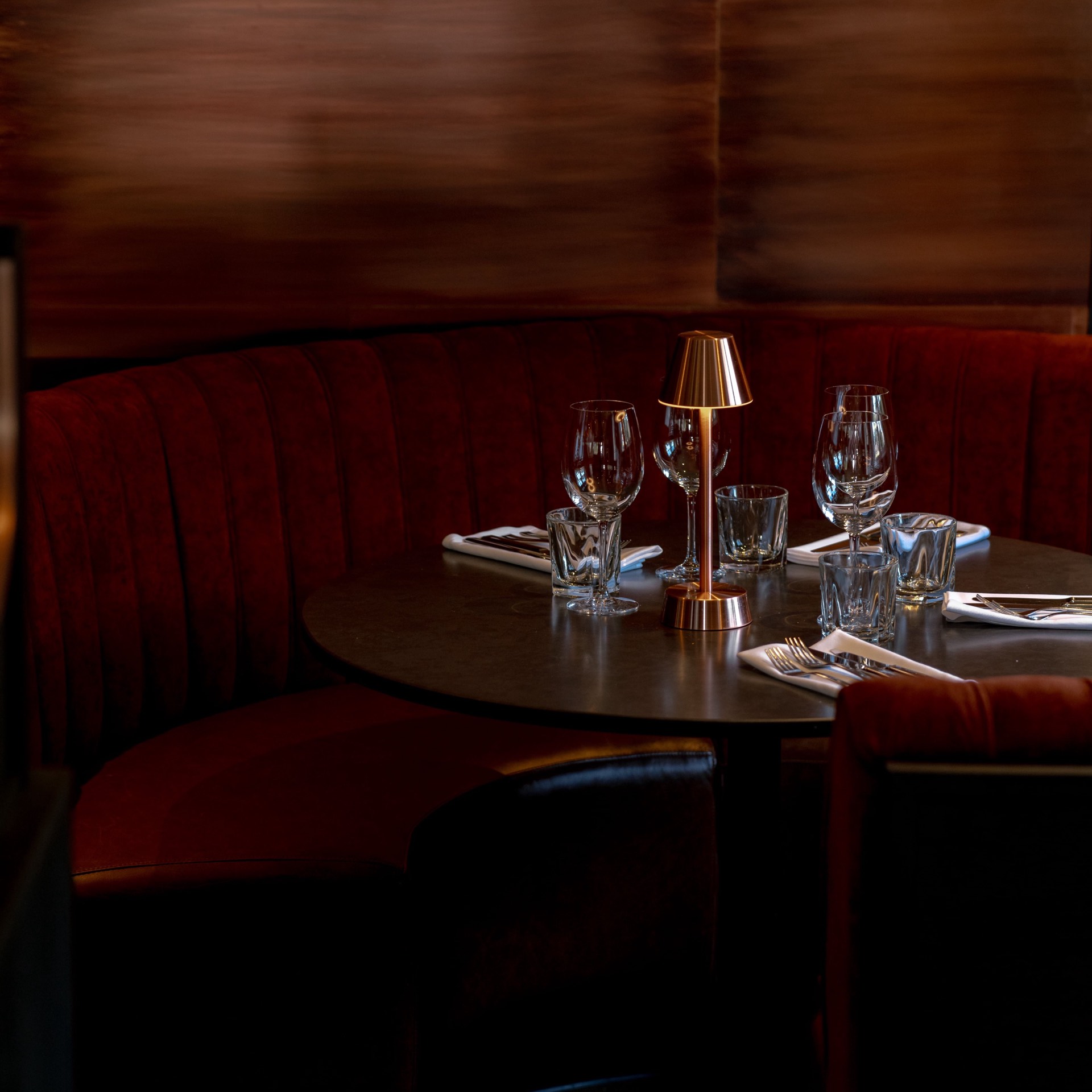 A restaurant booth with red velvet seating and a golden lamp