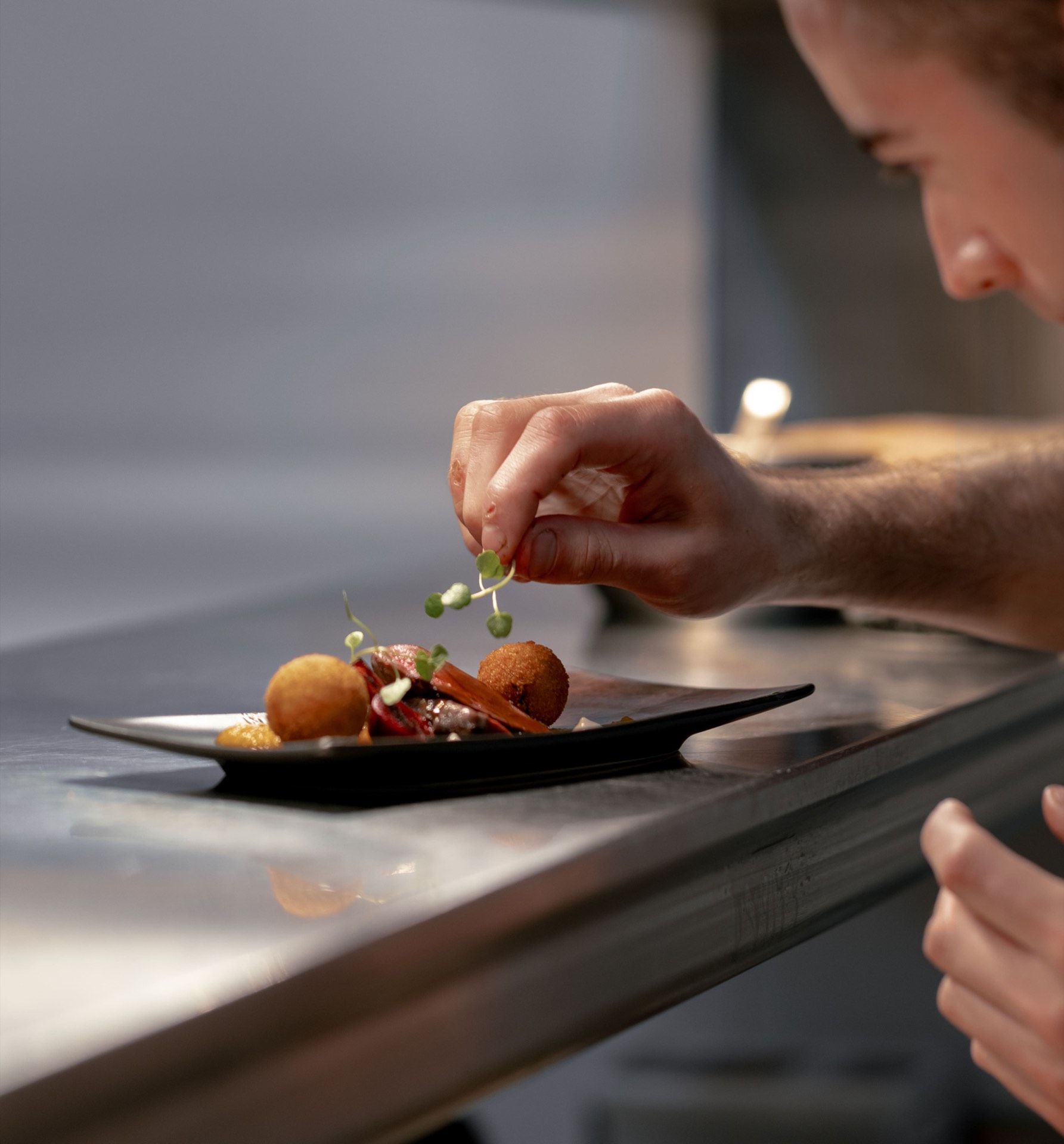 A chef garnishing a plated dish with fresh herbs