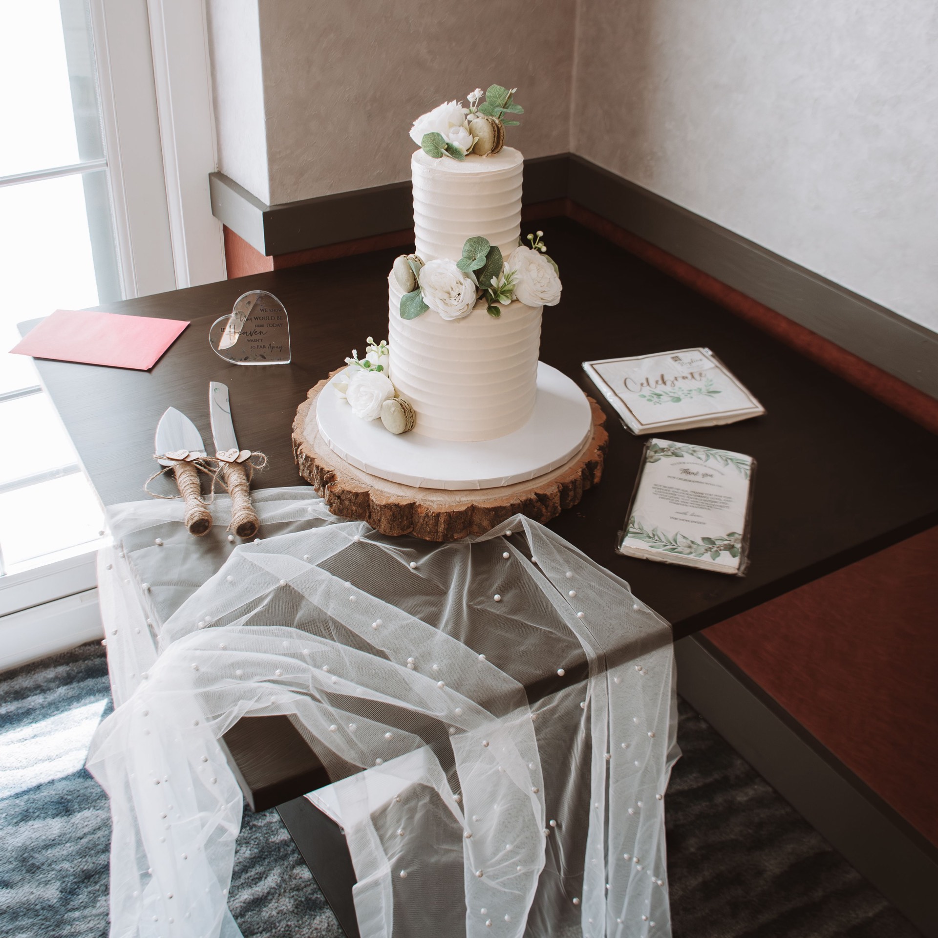An elegant two-tier white wedding cake decorated with white flowers and greenery on a wooden cake stand